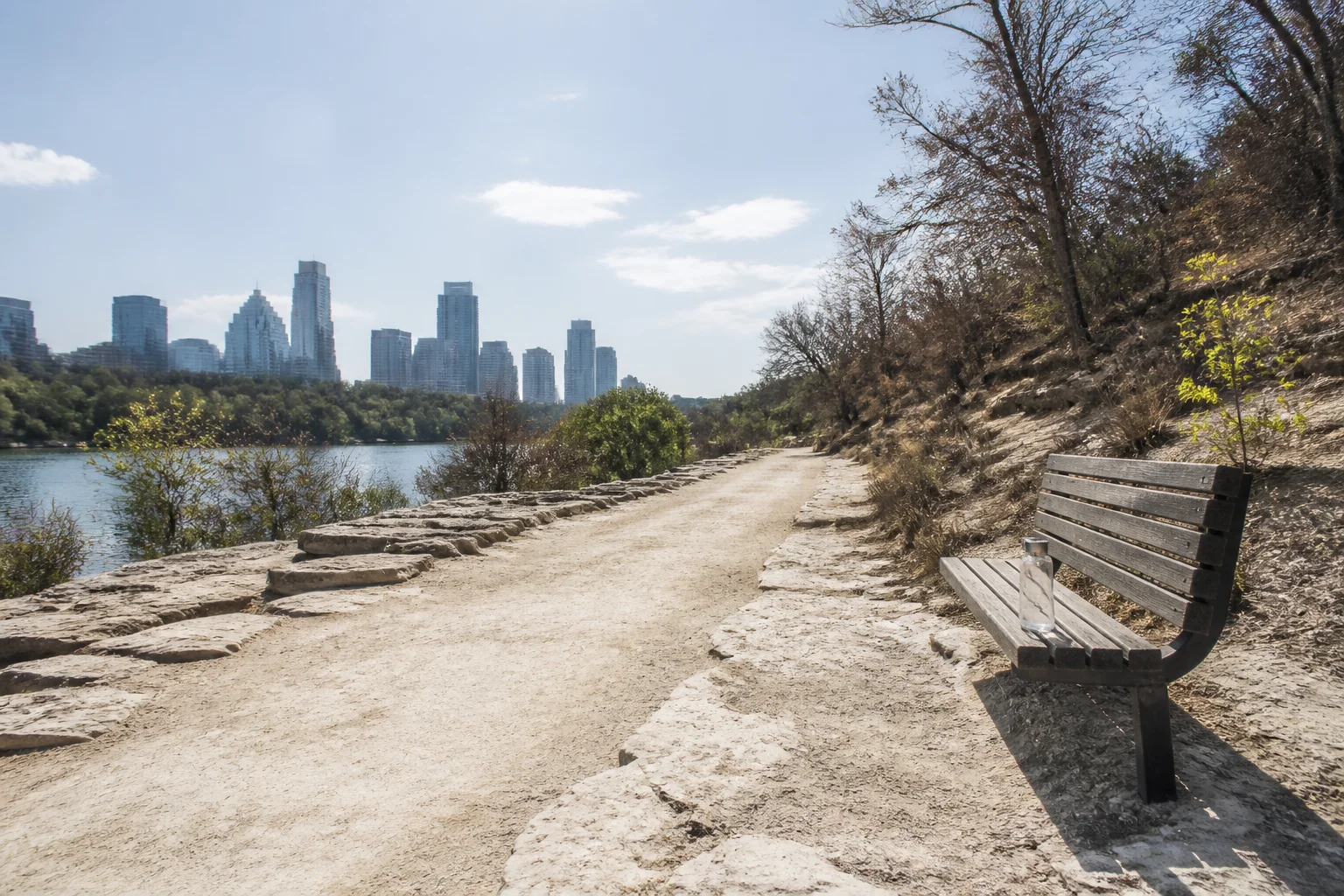 An empty sun-bleached trail and bench beside water under harsh midday heat near Austin